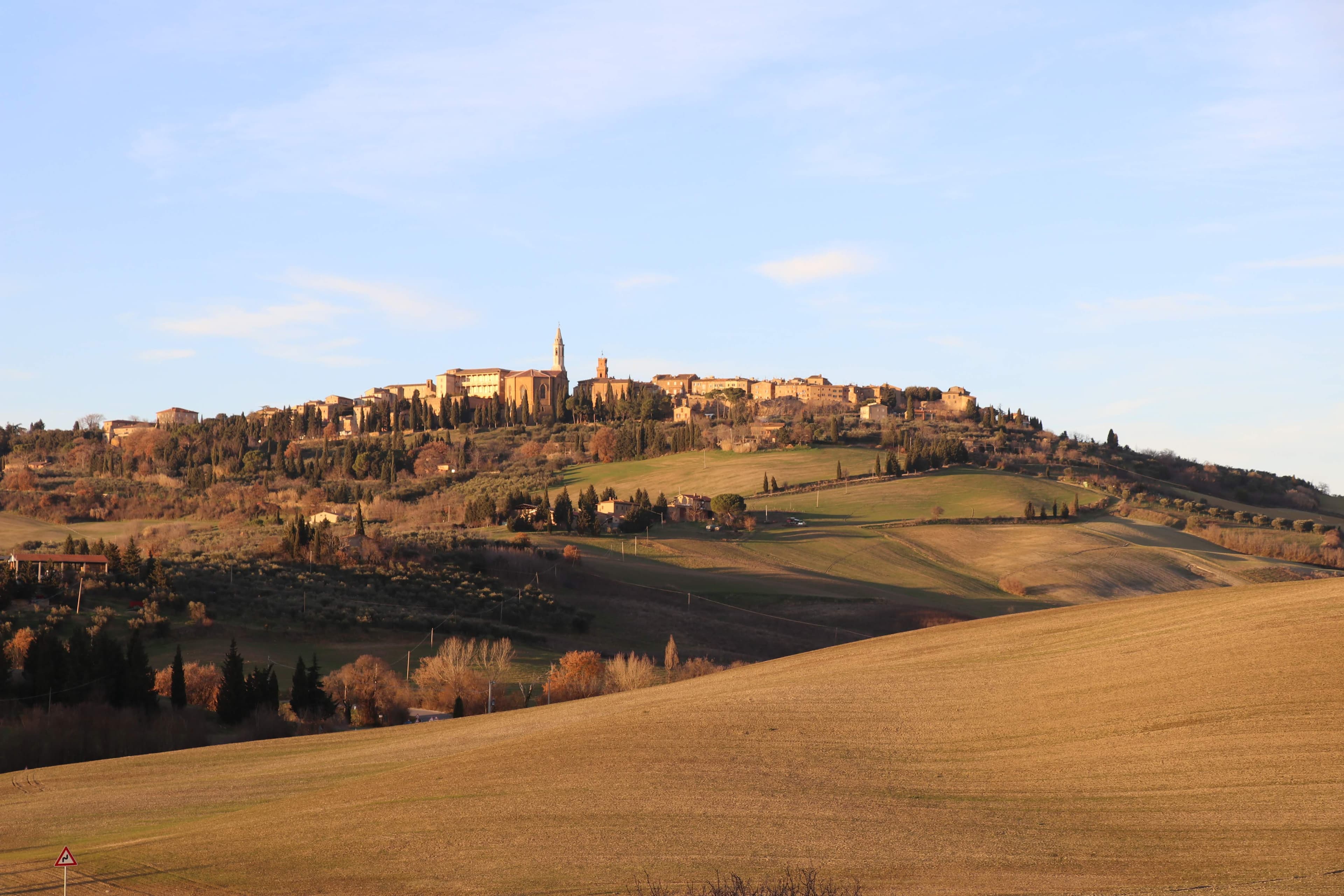 Pienza from the valley at golden hour — hilltop city above rolling fields
